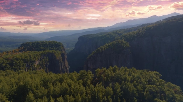 Vista superior de rochas altas na área montanhosa Céu do pôr do sol Nuvens roxas rosa As copas das árvores Foto de alta qualidade