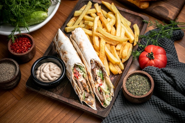 Vista superior de rolos de shawarma e batatas fritas a bordo e tomates uma tigela com tomilho em pano cinza