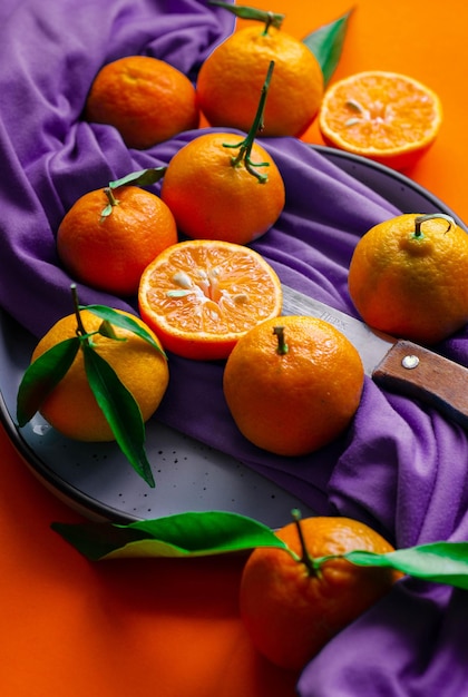 Vista superior de tangerinas frescas maduras ou orangers de tangerina com folhas verdes em fundo roxo.