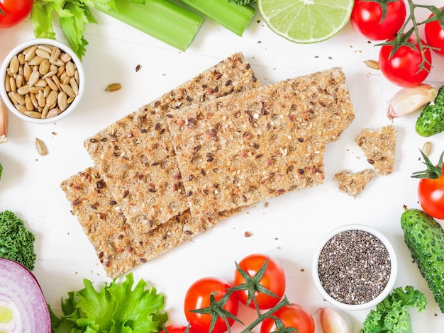 Vista superior de torradas de centeio de grãos inteiros rodeada de verduras frescas e sementes sobre fundo branco O conceito de comida orgânica e vegetariana