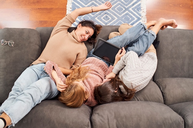 Vista superior de três amigas no sofá em casa olhando para um tablet