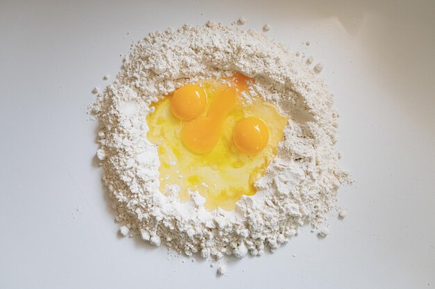 Vista superior de três ovos em uma pilha de farinha no balcão da cozinha