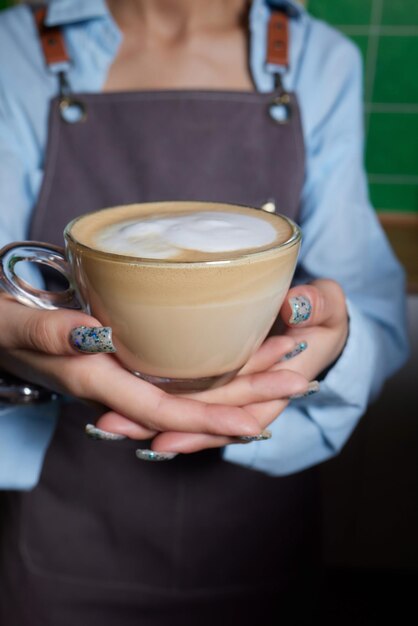Vista superior de um barista profissional derramando leite de um frasco em uma chávena de café. O café está sendo preparado por um barista. Foca nas mãos segurando uma chácara de café.