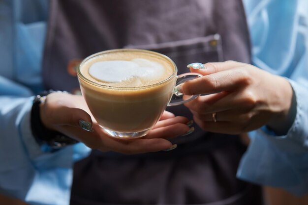 Vista superior de um barista profissional derramando leite de um frasco em uma chávena de café. O café está sendo preparado por um barista. Foca nas mãos segurando uma chácara de café.