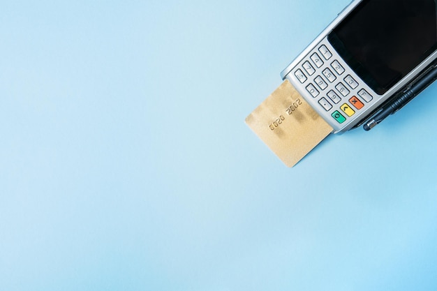 Foto vista superior de um cartão bancário perto de um terminal de pagamento em um conceito de pagamento sem contato de superfície azul