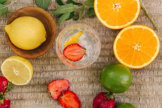 Vista superior de um copo alto com gelo de água e fatias de morango, frutas frescas na mesa de limão ao ar livre