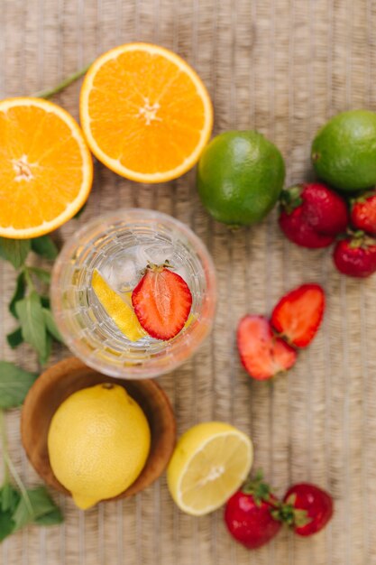Vista superior de um copo alto com gelo de água e fatias de morango, frutas frescas na mesa de limão ao ar livre