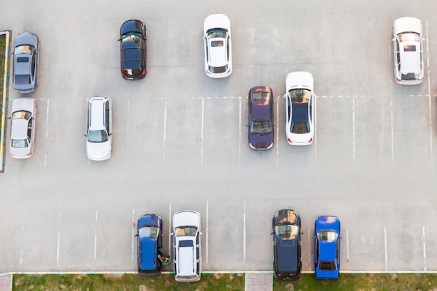 Vista superior de um estacionamento de asfalto semivazio com carros brancos e azuis pretos estacionados perto de um prédio residencial em um dia de verão