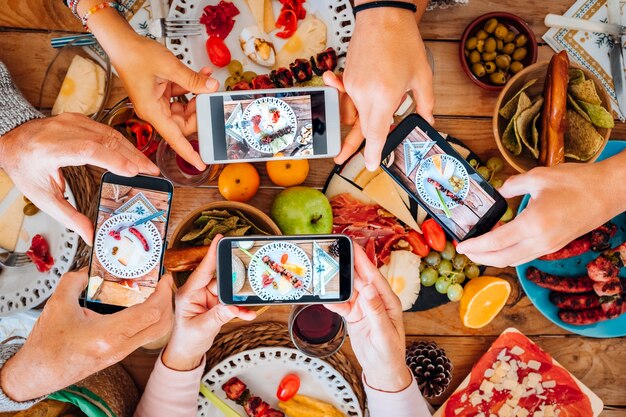 Vista superior de um grupo de pessoas durante a noite de Natal tirando fotos de comida e pratos com smartphone todos juntos