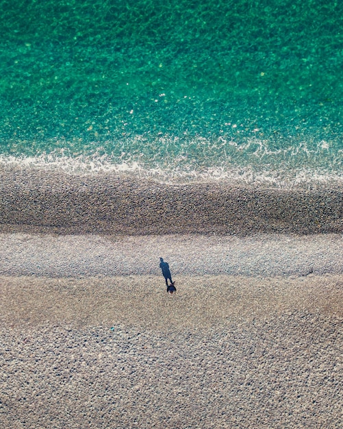 Vista superior de um homem solitário parado na costa do mar com bela água turquesa