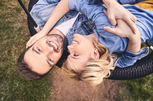 Vista superior de um homem sorridente e sua namorada bonita e alegre deitada em um balanço