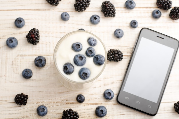 Foto vista superior de um iogurte com amoras, smartphone, frutas na mesa
