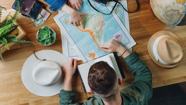 Vista superior de um jovem casal irreconhecível com mapas planejando viagem de férias