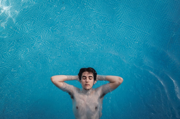 Vista superior de um jovem com os olhos fechados, flutuando em uma piscina com as mãos na nuca. Aproveitando as férias enquanto se bronzeava em um hotel. Conceito de férias.