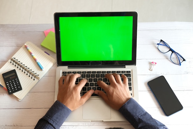 Vista superior de um jovem usando um laptop com uma tela em branco na mesa do escritório