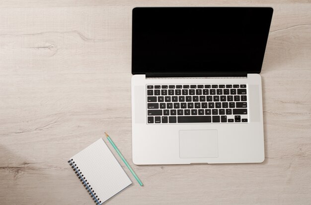 Vista superior de um laptop e um caderno com um lápis sobre um fundo claro de madeira, espaço para texto