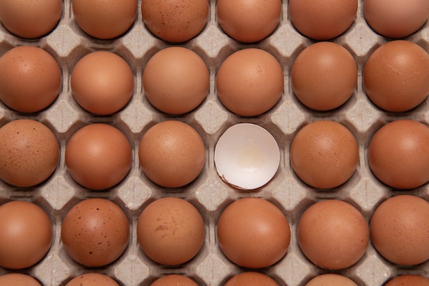 Vista superior de um ovo quebrado ao redor de muitos ovos na caixa
