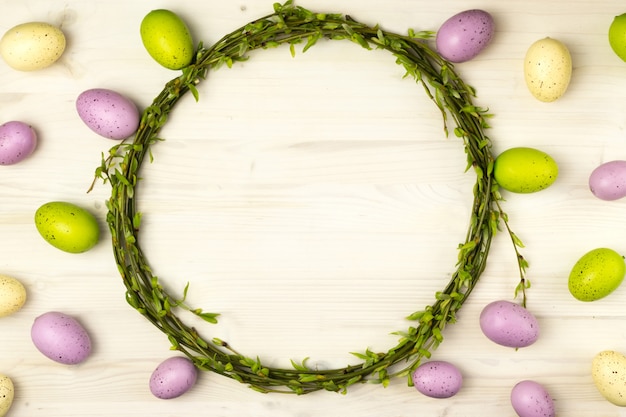 Vista superior de um ovos de Páscoa coloridos e coroa de salgueiro de primavera em um fundo de madeira claro com espaço de mensagem