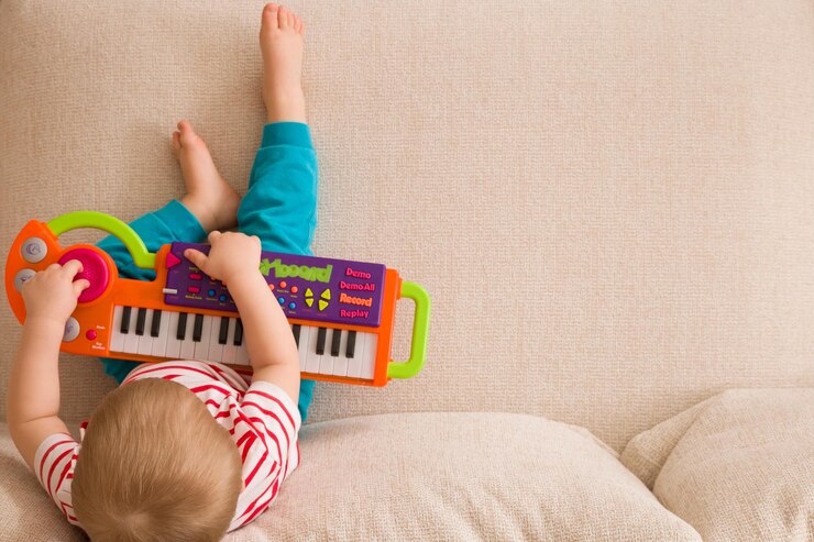 Vista superior de um pequeno menino bonito sentado no sofá e tocando no piano de brinquedo