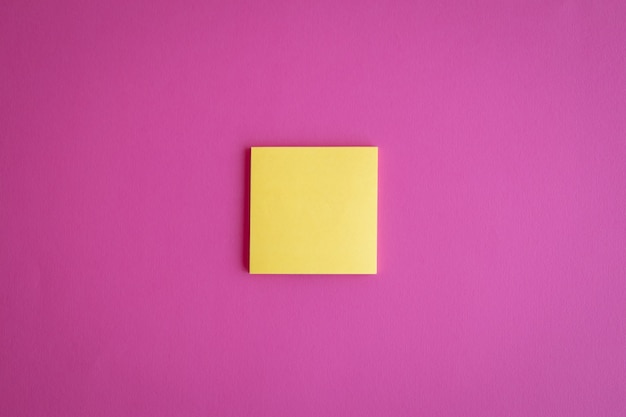 Vista superior de um post-it de papel em branco amarelo em um fundo rosa com um espaço de cópia