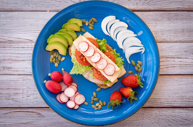 Vista superior de um prato azul com um sanduíche saudável e dietético com carne de peru e vegetais - alimentação saudável e saborosa - pão integral com sementes