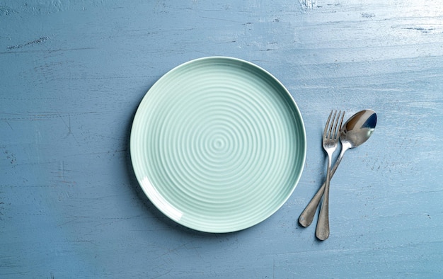 Vista superior de um prato com um garfo e uma colher em uma mesa de madeira azul