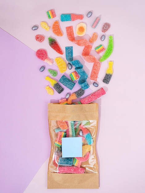Foto vista superior de um saco de kraft com marmelada de goma de mascar espalhada em um fundo lila na forma de diferentes figuras engraçadas