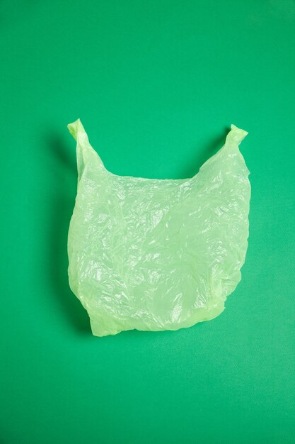 Foto vista superior de um saco plástico simples amassado colocado sobre um fundo verde brilhante no estúdio