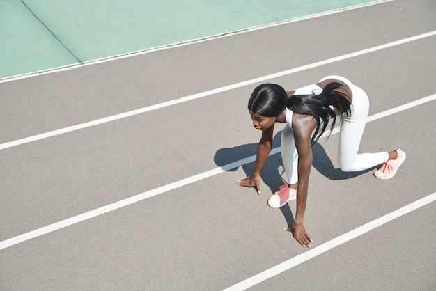 Vista superior de uma bela jovem africana em pé na posição inicial na pista de corrida ao ar livre