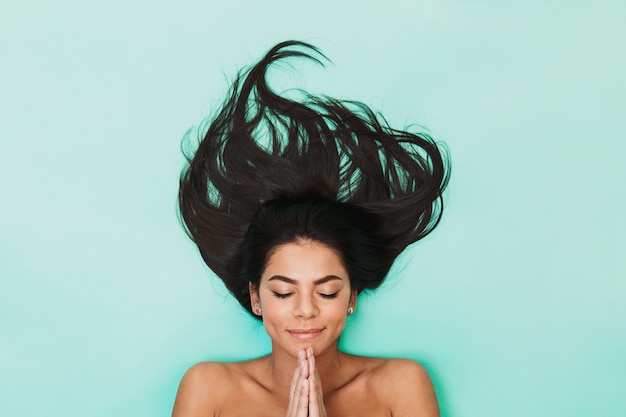 Vista superior de uma bela jovem morena de topless com cabelo comprido deitado sobre o azul