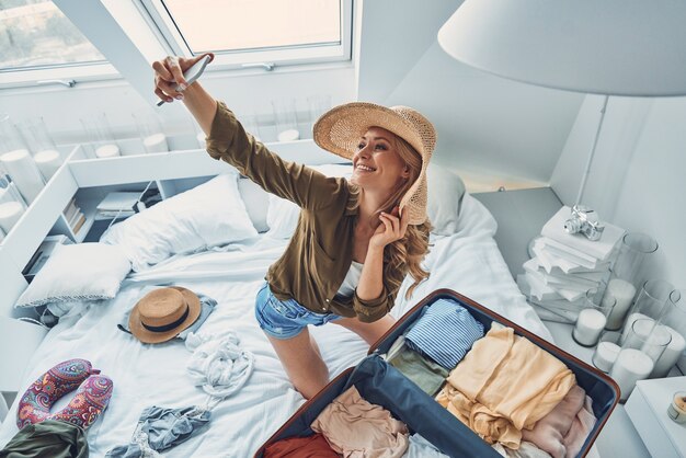 Foto vista superior de uma bela jovem sorridente fazendo selfie enquanto arruma a bagagem em casa