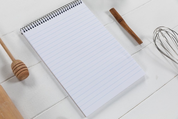 Vista superior de uma composição com uma página vazia em um caderno com colher de pau e bigode, disposta sobre uma superfície de madeira texturizada branca