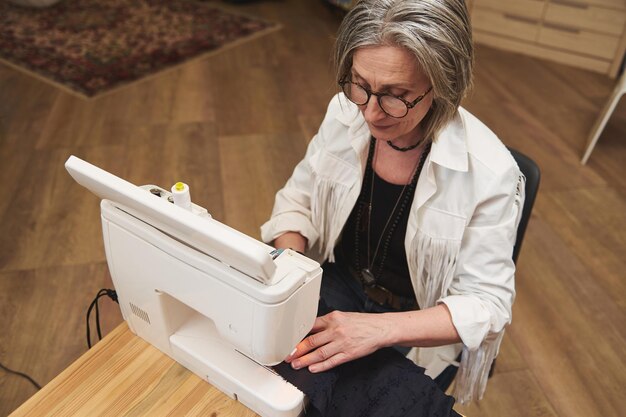 Vista superior de uma costureira elegante mulher madura costurando roupas em uma máquina de costura em um atelier de costura para criar e reparar roupas