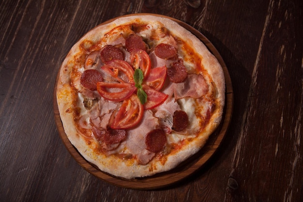 Vista superior de uma deliciosa pizza com fatias de salame e presunto servido na mesa de madeira