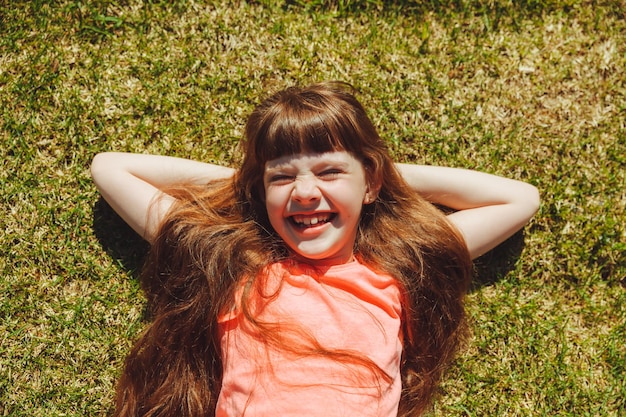 Vista superior de uma garota feliz sorrindo e deitada na grama verde em um dia de verão no parque