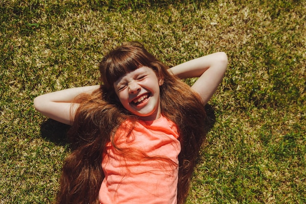 Vista superior de uma garota feliz sorrindo e deitada na grama verde em um dia de verão no parque