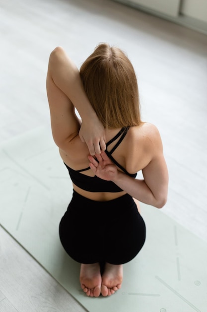 Vista superior de uma jovem calma em roupas esportivas está fazendo exercícios no tapete de ioga.