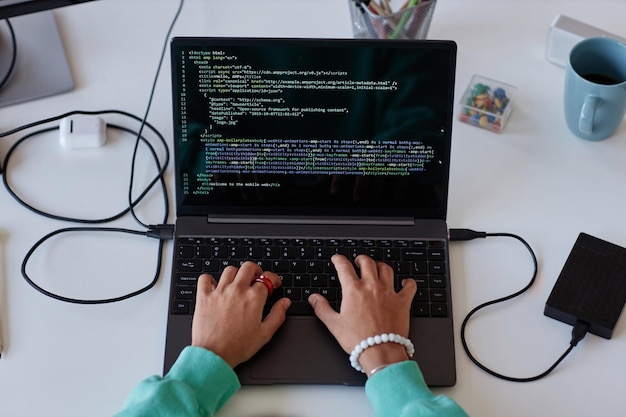 Vista superior de uma jovem escrevendo códigos de computador no laptop enquanto está sentada em seu local de trabalho