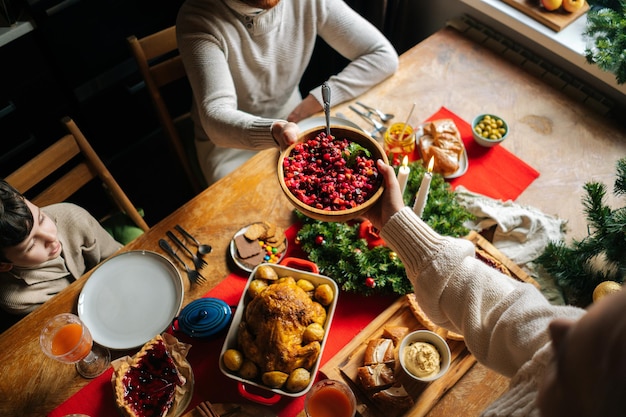 Vista superior de uma jovem feliz e um homem passando uma comida deliciosa sentado à mesa festiva de Natal com