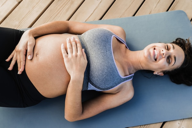 Vista superior de uma jovem grávida fazendo ioga ao ar livre - foco nas mãos segurando a barriga