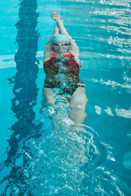 Vista superior de uma jovem nadadora treinando na piscina nadando de costas debaixo d'água Flutua debaixo d'água e sopra anéis de ar
