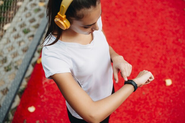 Vista superior de uma jovem olhando para o relógio esportivo depois de fazer cardio e ouvir música ao ar livre em um parque esportivo.