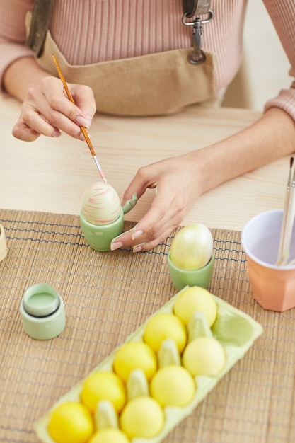 Vista superior de uma jovem pintando ovos em cores pastel para a Páscoa enquanto está sentado à mesa na cozinha, copie o espaço