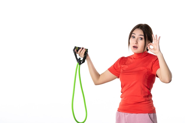 Vista superior de uma jovem surpresa ajeitando ordenadamente o cabelo vestido na blusa de redorange e segurando o acessório esporte corda fazendo gesto de óculos em fundo branco