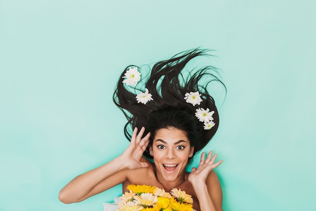 Foto vista superior de uma linda jovem morena com cabelo comprido deitado sobre o azul, segurando um buquê de flores