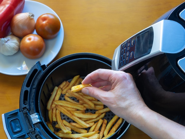 Vista superior de uma mão colhendo uma batata frita de uma fritadeira com um prato de legumes Conceito de comida saudável