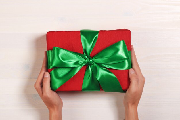 Vista superior de uma mão segurando uma caixa vermelha com um presente com uma fita verde.