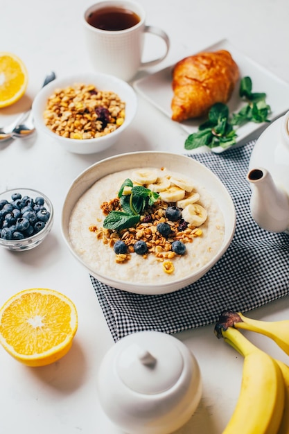 Vista superior de uma mesa branca com farinha de comida com frutas e nozes frutas bagas chá hortelã laranjas bananas pratos de chaleira com espaço livre