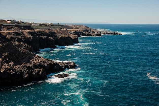 Vista superior de uma montanha com uma pequena cidade de um mar profundo e brilhante com ondas sob o céu azul claro em um dia ensolarado