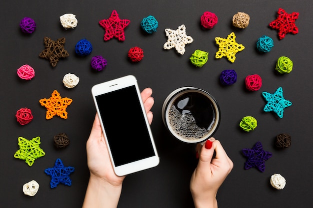 Vista superior de uma mulher segurando um telefone em uma mão e uma xícara de café em outra mão no preto.